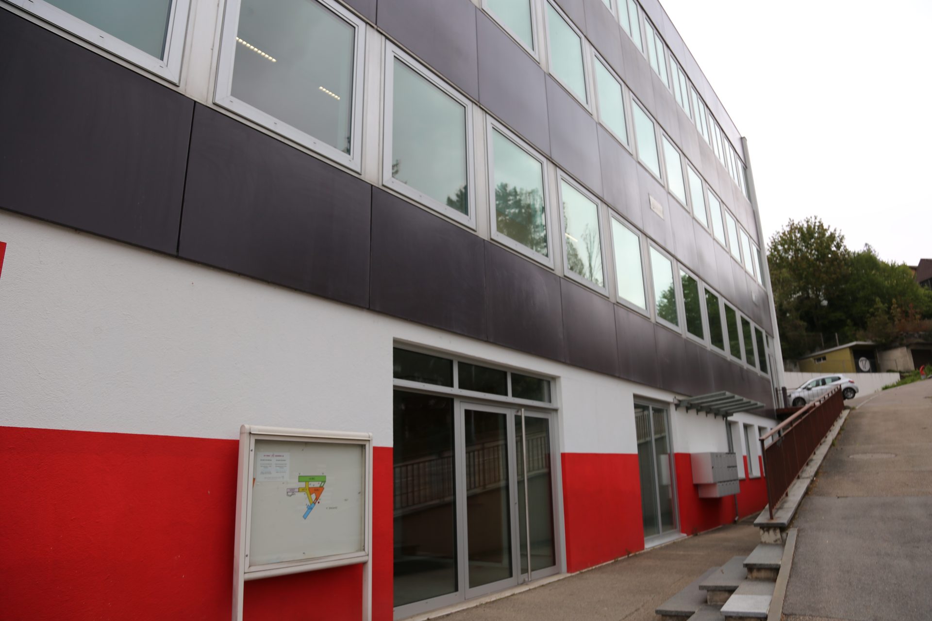 Vista esterna dell'edificio dello studio con facciata grigio-bianco-rossa, ingresso in vetro e rampa laterale