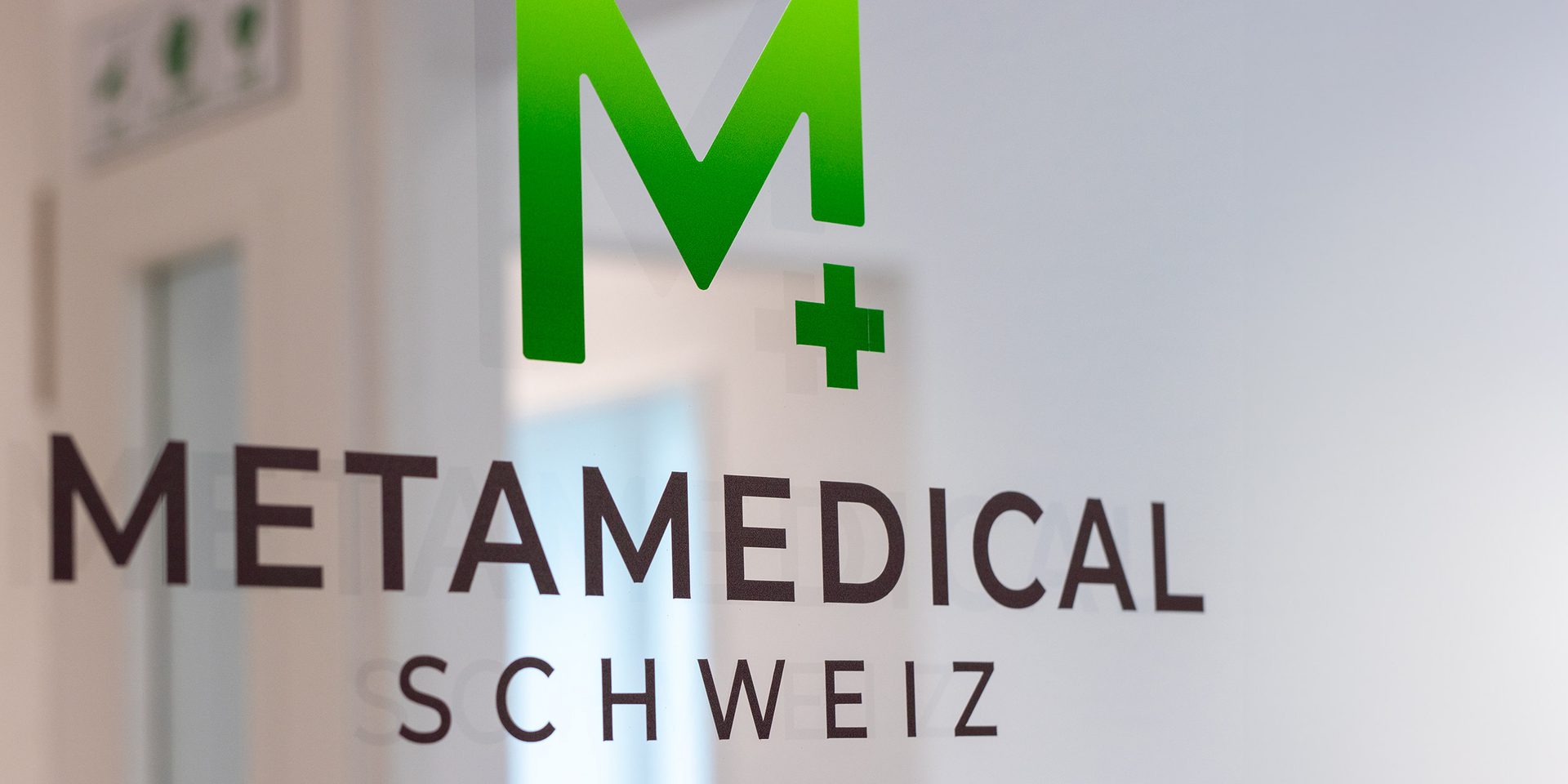 Logo Metamedical Schweiz sulla porta a vetri all'ingresso dello studio, dietro l'area interna luminosa